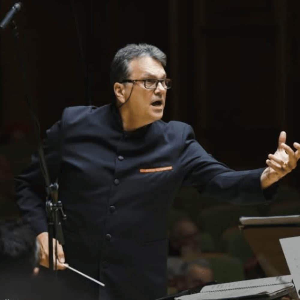 Conductor in a dark suit leading a performance with a baton and expressive hand gestures.